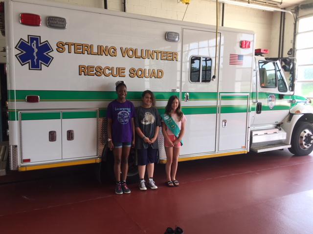 3 girls from Girl Scout Troop 789 standing infront of an ambulance